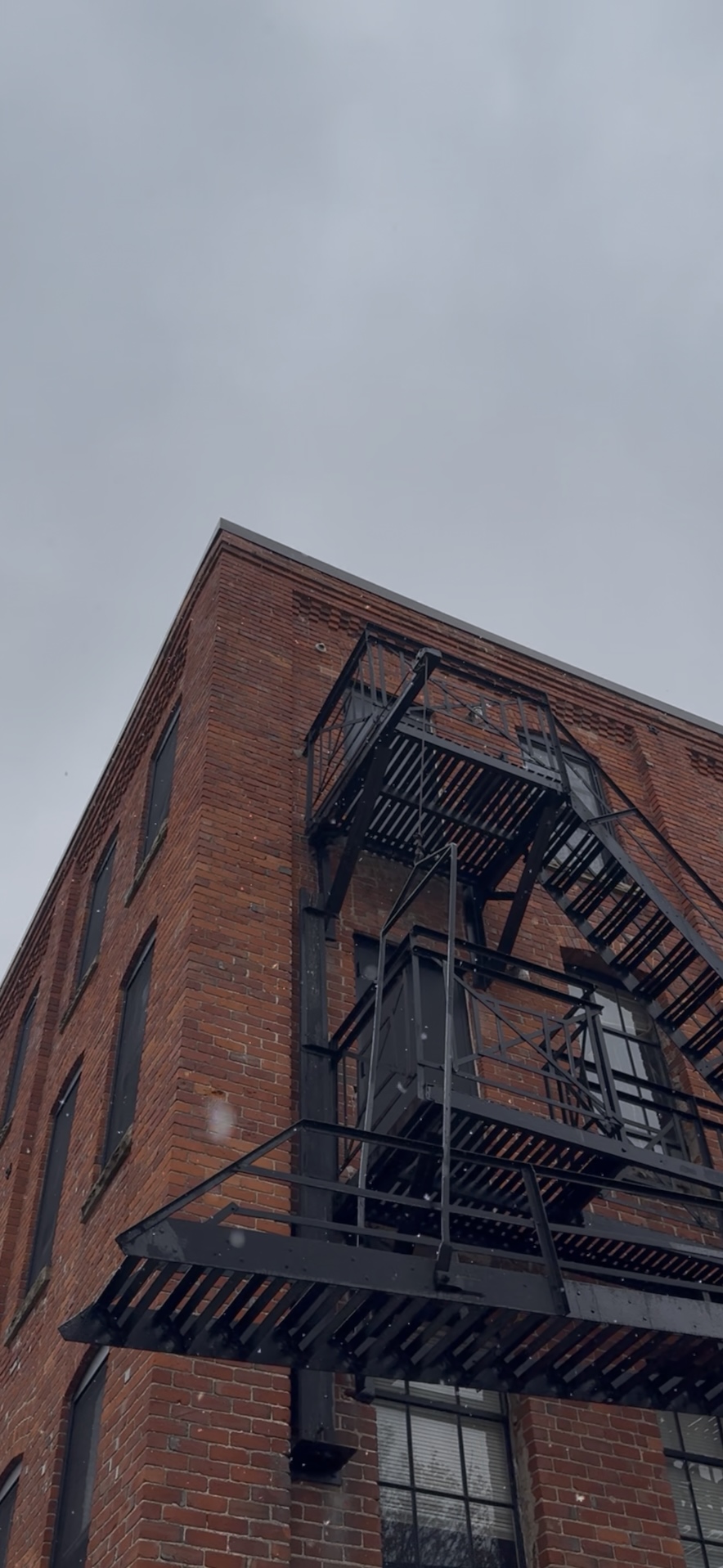 Snow falling in front of the Argus Museum building; grey skies in the background.